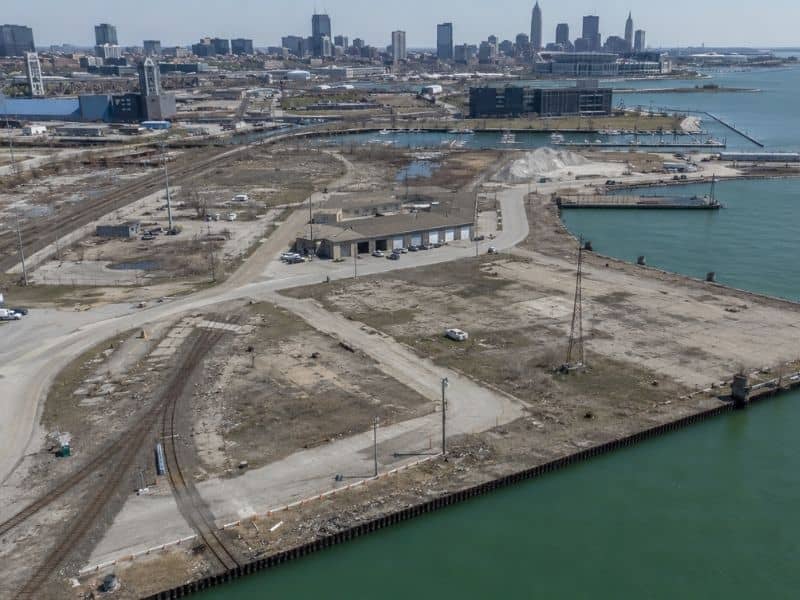 Aerial view of a Cleveland lakefront redevelopment site with rail lines, roads, parking areas, utilities, and shoreline improvements