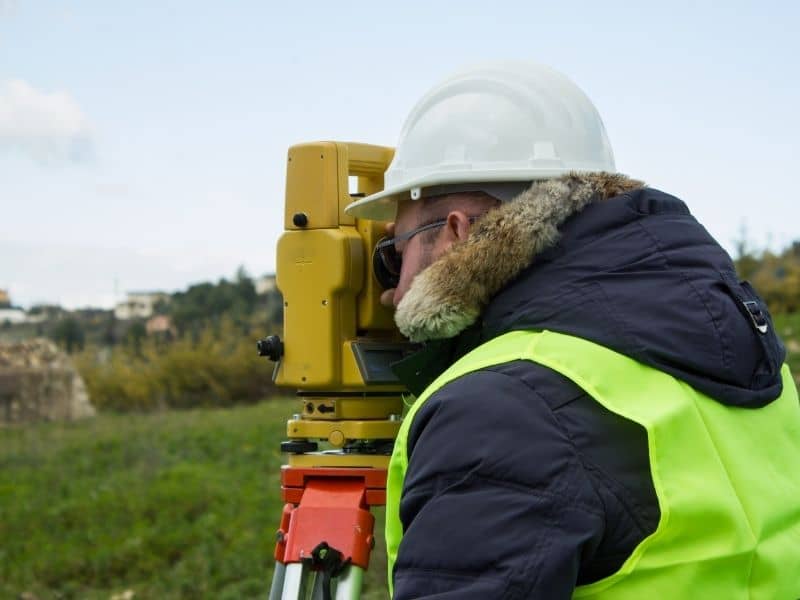 Surveyor using equipment to check boundary lines on open land before housing development.